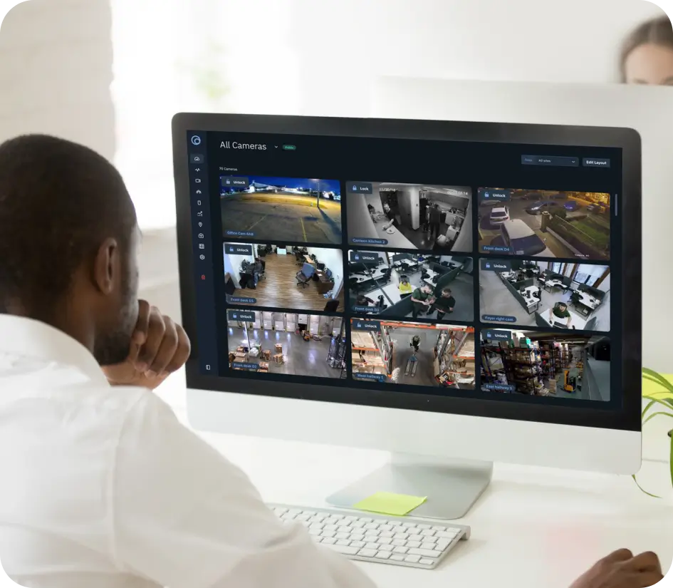 Man watching a multi-camera surveillance feed on a large monitor in an office setting, monitoring security footage.
