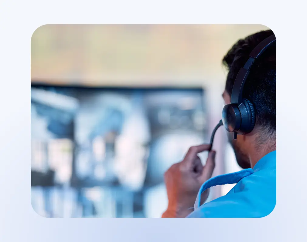 Person wearing a headset and speaking into a microphone in a control room or monitoring station.