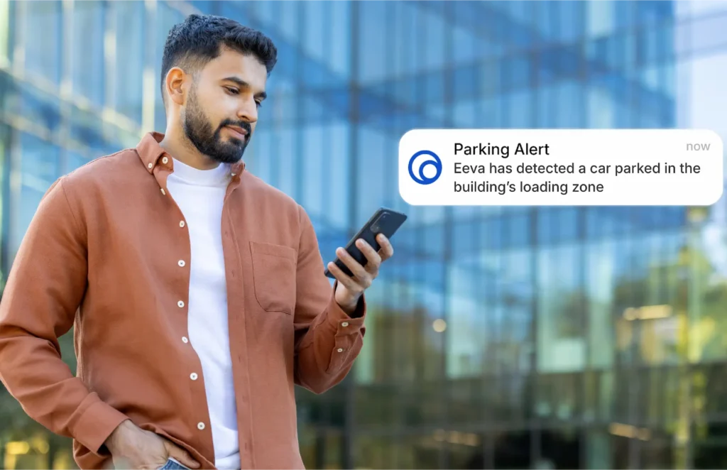 Man outdoors checks his phone as a Parking Alert pops up: a car is in the building's loading zone.