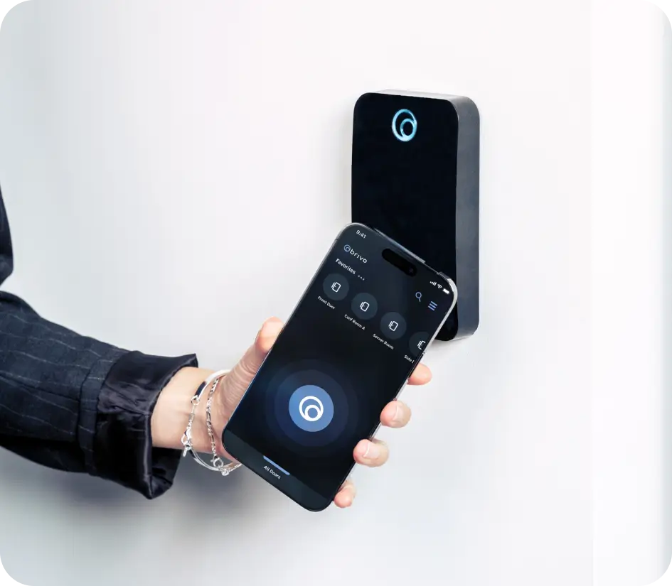 Person holding a smartphone near a wall-mounted smart lock, using a control app on the screen.