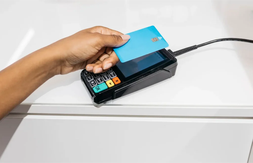 Person inserts a blue credit card into a handheld payment terminal connected by a cable.