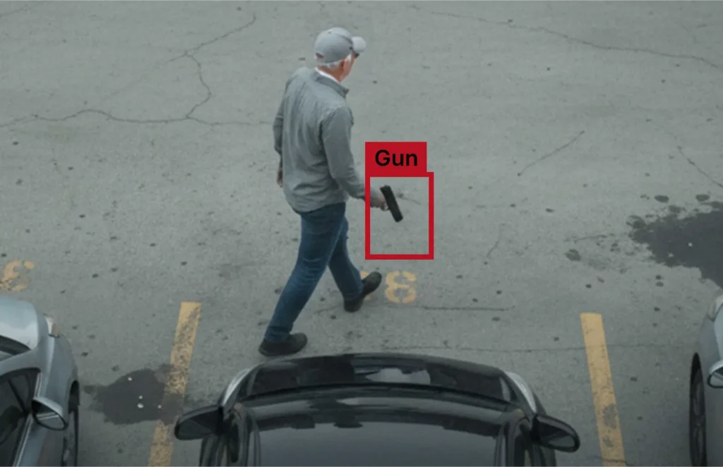 Man walking in a parking lot while holding a handgun in his right hand (surveillance image).
