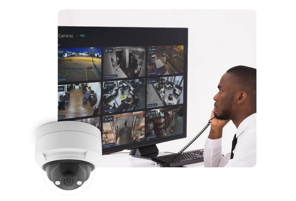 Control room with a multi-camera CCTV monitor showing live feeds; a security officer wearing a headset sits nearby.