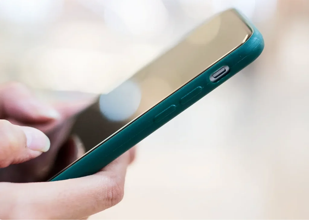 Close-up of a teal smartphone held in hands, showing the side button and curved edge near the screen.