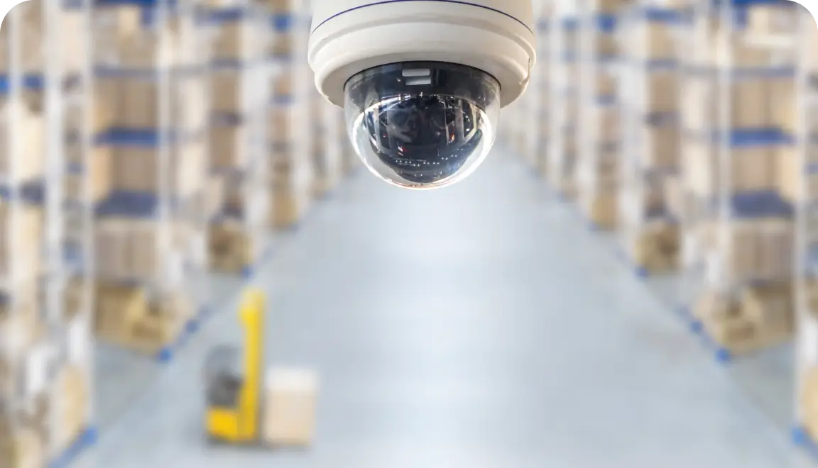 Security camera overlooking a warehouse aisle with tall shelves in the background.