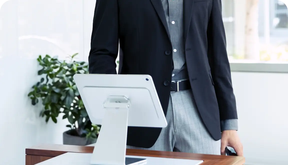 Businessperson in a dark blazer stands at a reception desk with a tablet on a stand in front of them.