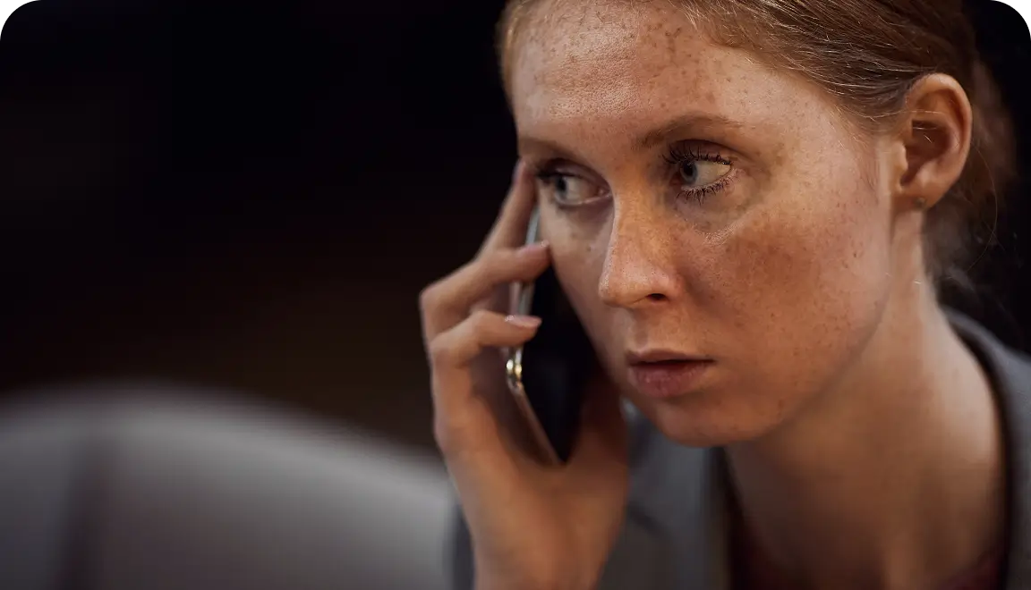 Close-up of a freckled woman talking on a smartphone, looking to the side with a focused expression.