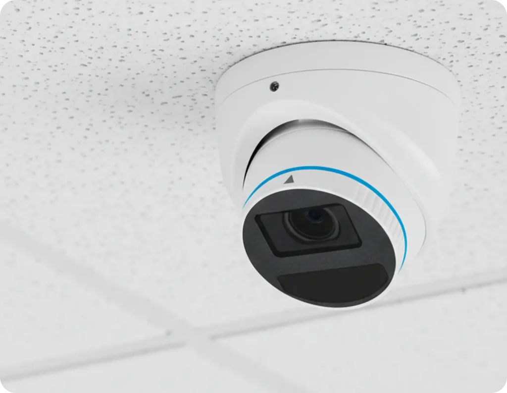 White dome surveillance camera mounted to a textured ceiling, angled downward to monitor the area