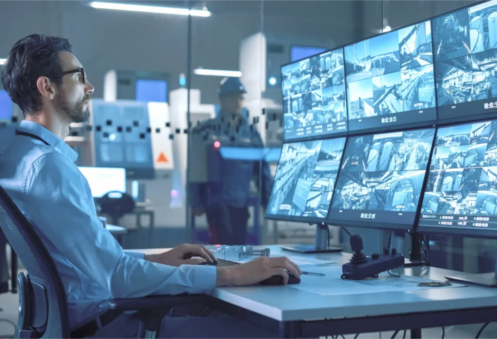 Operator seated at a security workstation, monitoring a wall of CCTV feeds on multiple screens in a high-tech control room.
