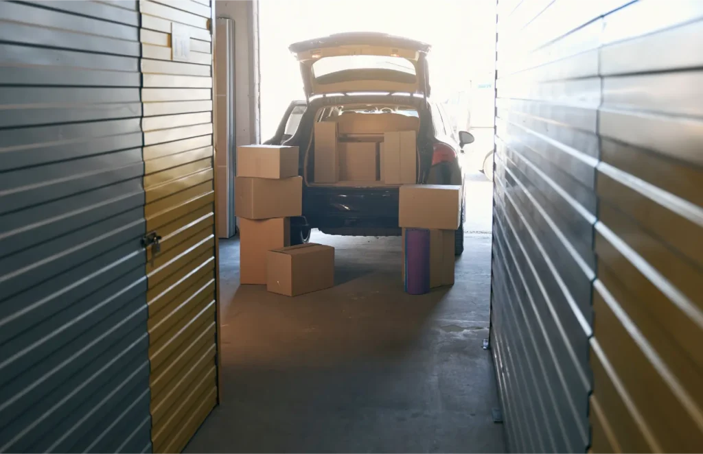 SUV with rear hatch open, loaded with cardboard boxes in a storage unit between metal shelves.