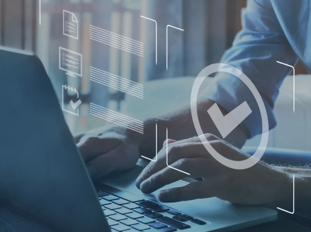 Unas manos tecleando en un portátil con un icono grande de una marca de verificación que indica aprobación o éxito en un flujo de trabajo digital.
