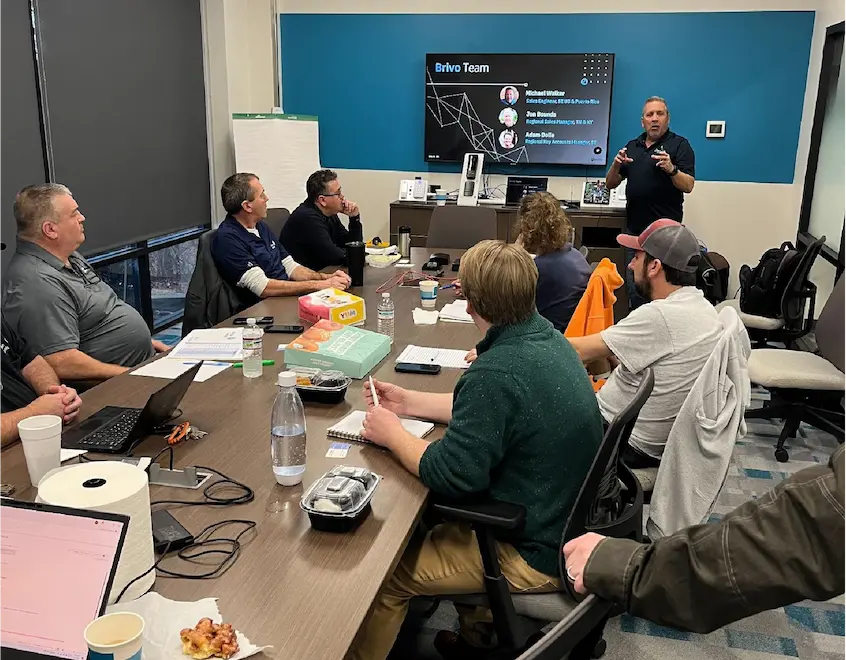 Team in a conference room watching a presenter at the front; screen shows 'Brivo Team' slide.